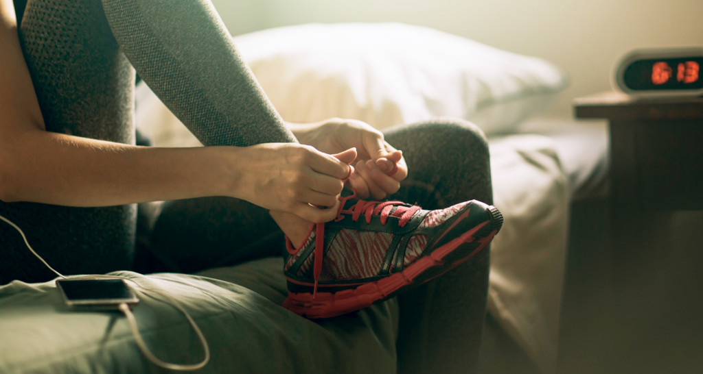 Woman tying running shoes on bed