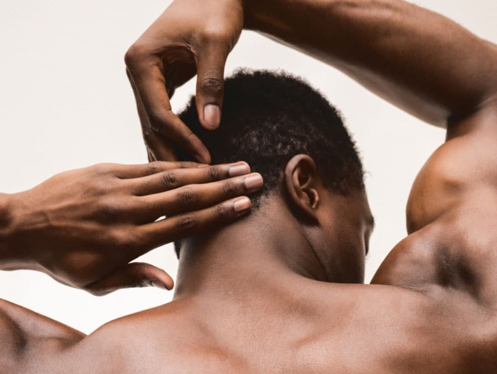 Man's back without a shirt on while he's rubbing his neck