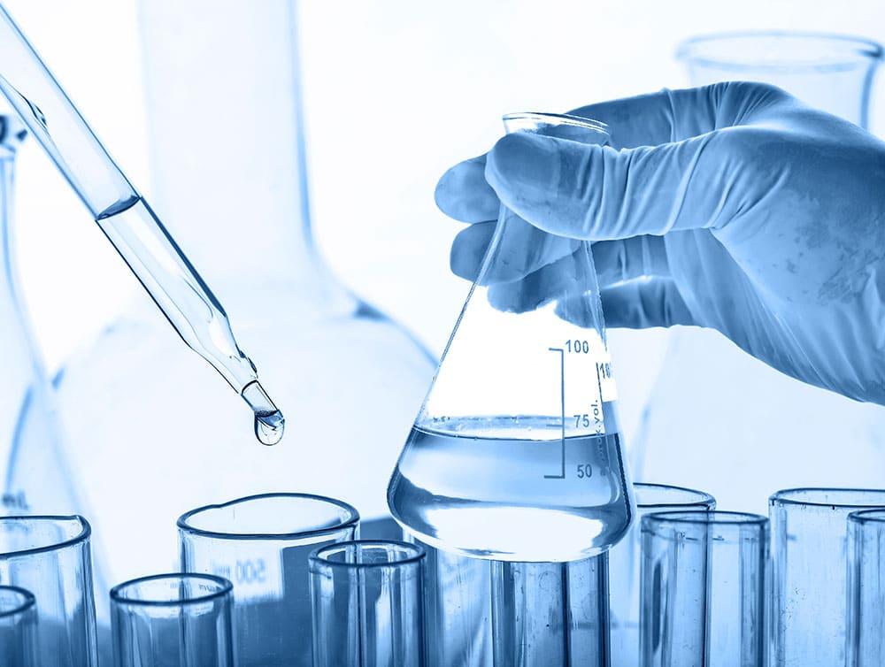 Scientist in lab with beakers and test tubes with clear liquid in beaker