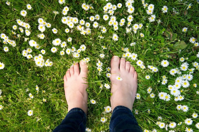 Female,Feet,Standing,On,Green,Grass,And,White,Flowers,-