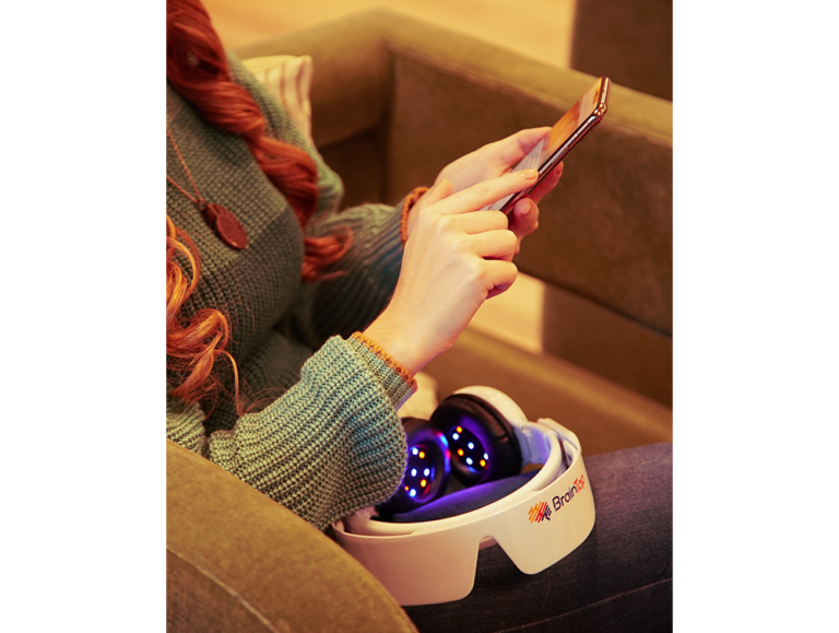 Person holding the BrainTap device on their lap while looking at the app on a smartphone