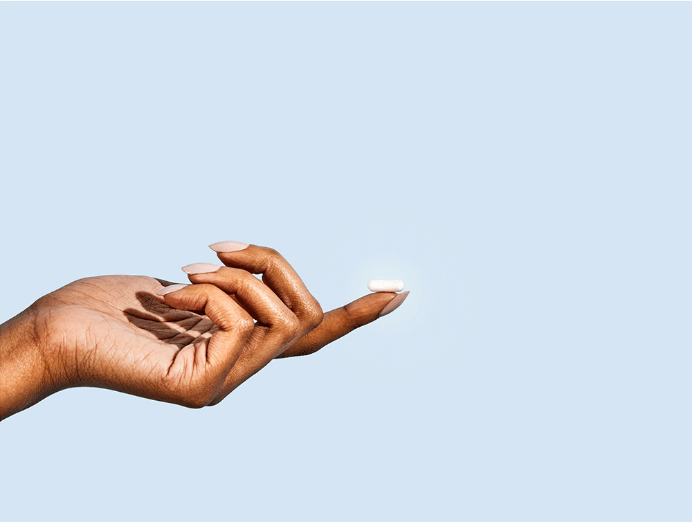 Person holding a white supplement on their finger tip.