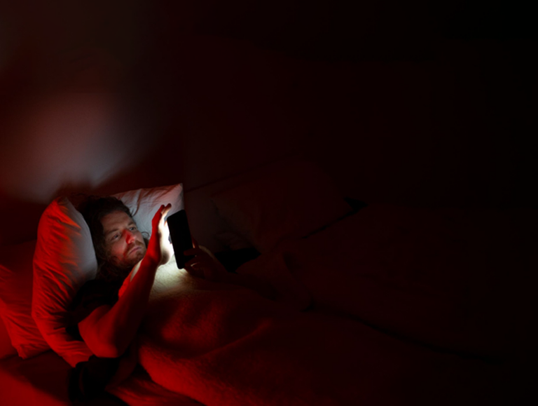 Man laying in bed reading from a smartphone